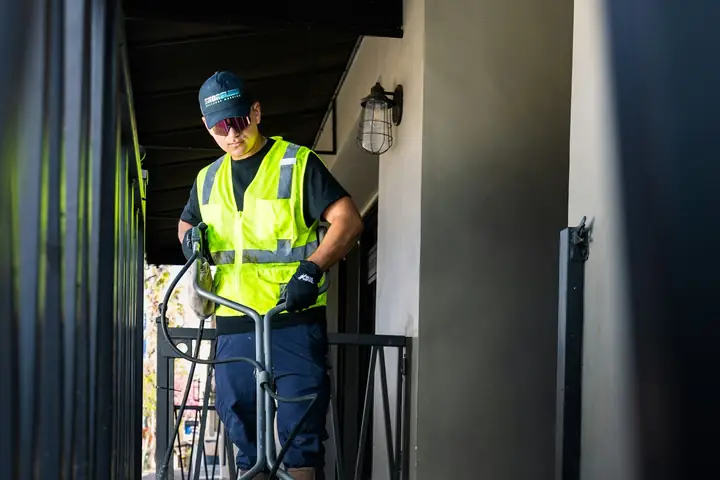 Worker in high-visibility vest pressure washing a building entrance